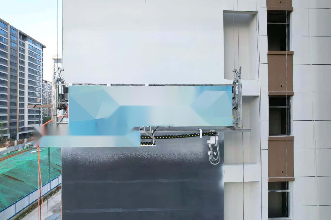 Facade hanging painting robot suspended below a gondola spraying a high-rise concrete facade